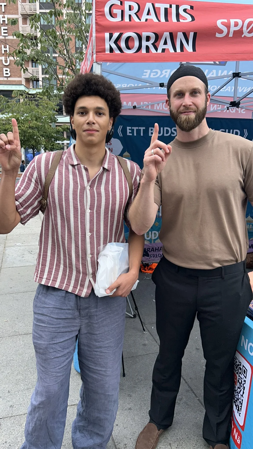 Two people standing beside a tent displaying a free Quran sign