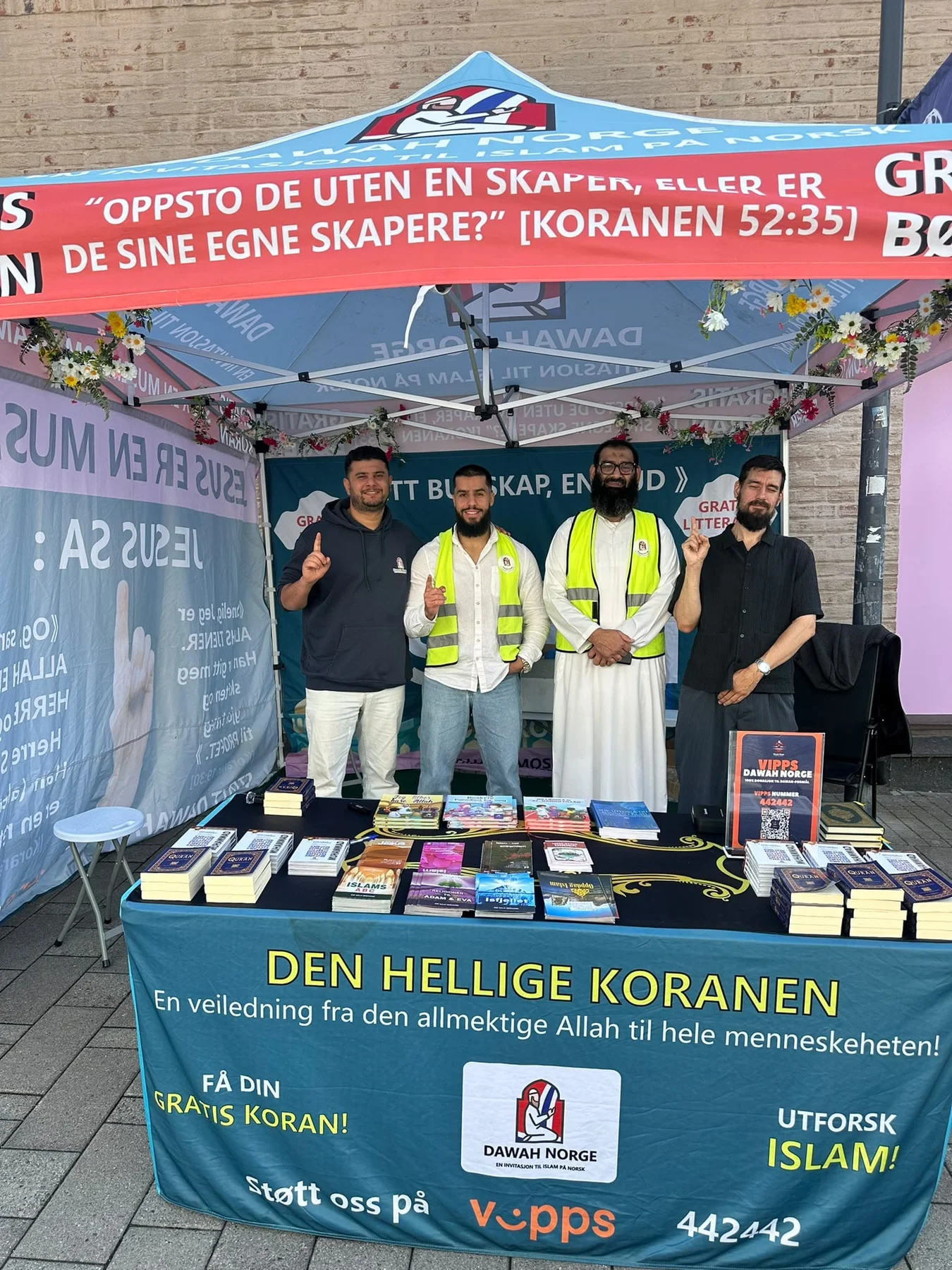 Four people behind a table of Qurans and books at the Dawah Norway tent in Fredrikstad