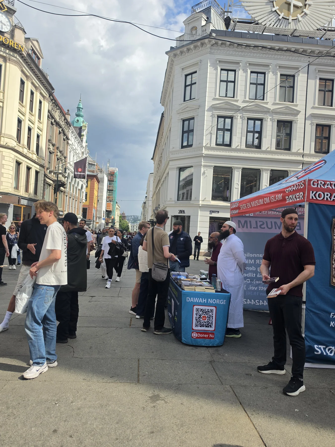 People talking beside a Dawah Norway information tent on a busy street in Oslo