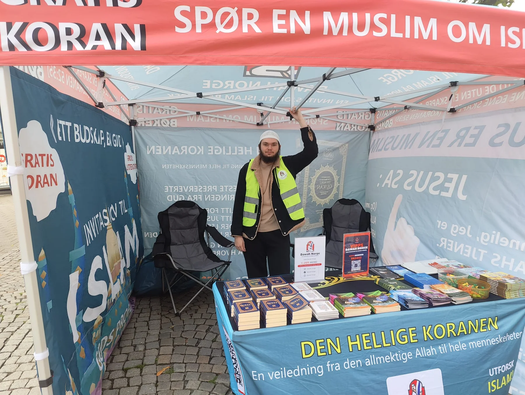 A person standing behind Qurans and books inside the Dawah Norway tent in Stavanger
